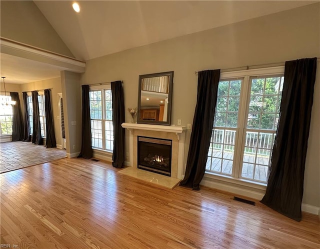 unfurnished living room with plenty of natural light, high vaulted ceiling, a chandelier, and light hardwood / wood-style flooring