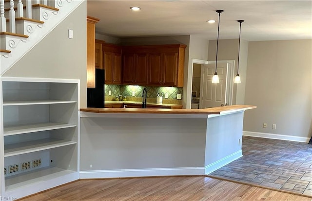 kitchen featuring black refrigerator, tasteful backsplash, sink, pendant lighting, and light hardwood / wood-style flooring