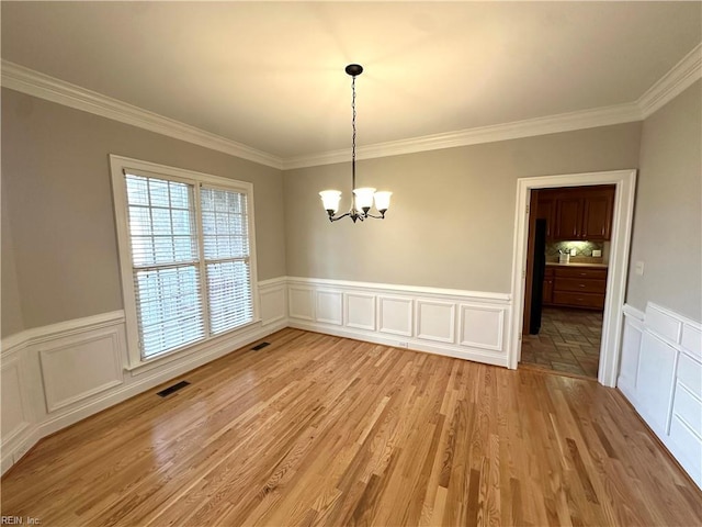 unfurnished dining area with a notable chandelier, light hardwood / wood-style floors, and crown molding