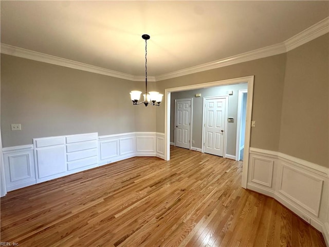 unfurnished dining area with crown molding, an inviting chandelier, and light wood-type flooring