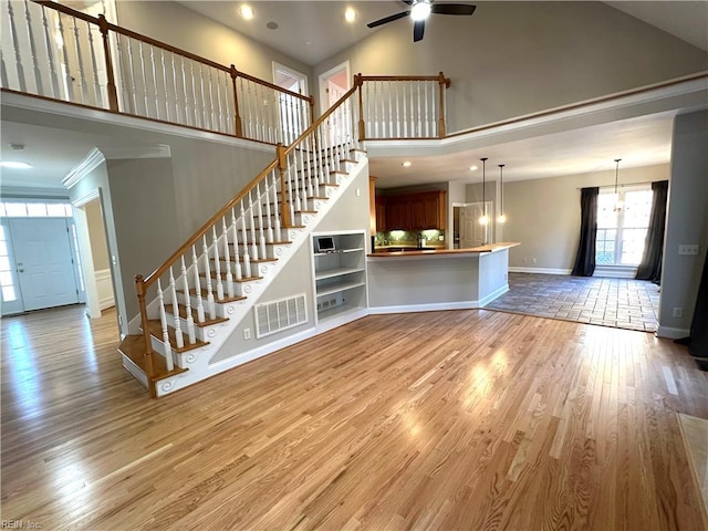 unfurnished living room with ceiling fan with notable chandelier, ornamental molding, a high ceiling, and light wood-type flooring