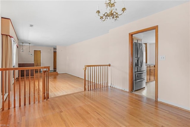 spare room featuring a chandelier and light wood-type flooring