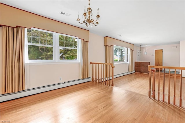 empty room featuring light wood-type flooring, a baseboard radiator, and a chandelier