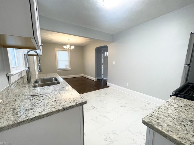 kitchen with stainless steel refrigerator, light stone countertops, sink, hanging light fixtures, and a chandelier