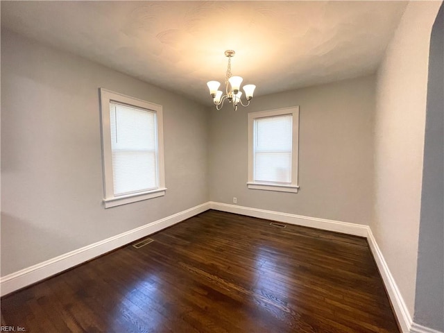 spare room with a notable chandelier and dark hardwood / wood-style flooring