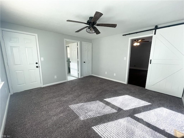 unfurnished bedroom featuring connected bathroom, a barn door, ceiling fan, and dark carpet