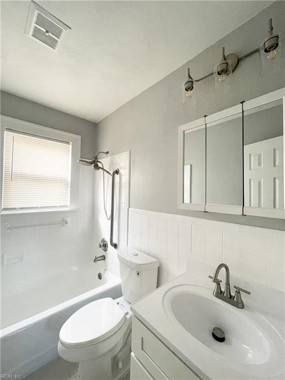 full bathroom with vanity, tiled shower / bath combo, toilet, and tile walls