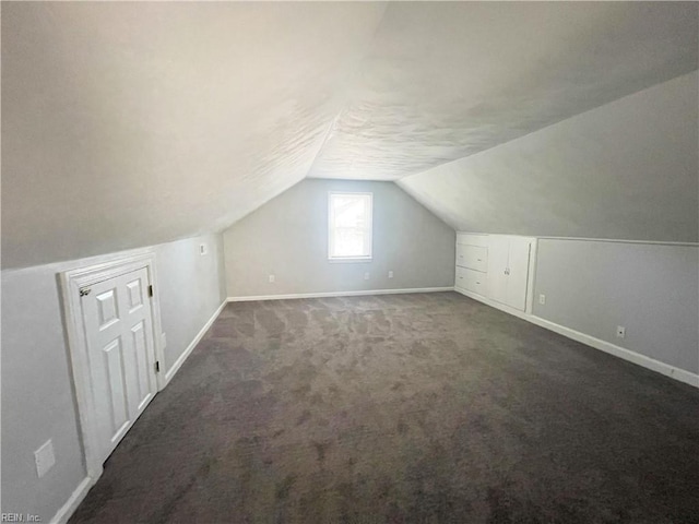 bonus room with dark carpet and vaulted ceiling