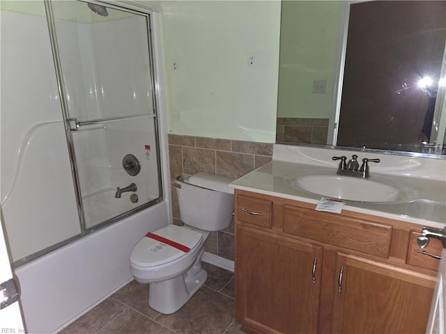 full bathroom featuring tile patterned flooring, toilet, shower / bath combination with glass door, vanity, and tile walls