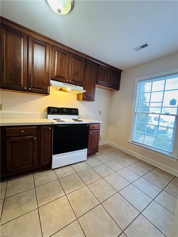 kitchen with light tile patterned floors, white range with electric stovetop, visible vents, light countertops, and under cabinet range hood