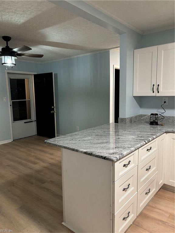 kitchen featuring kitchen peninsula, light stone countertops, light hardwood / wood-style flooring, and white cabinets