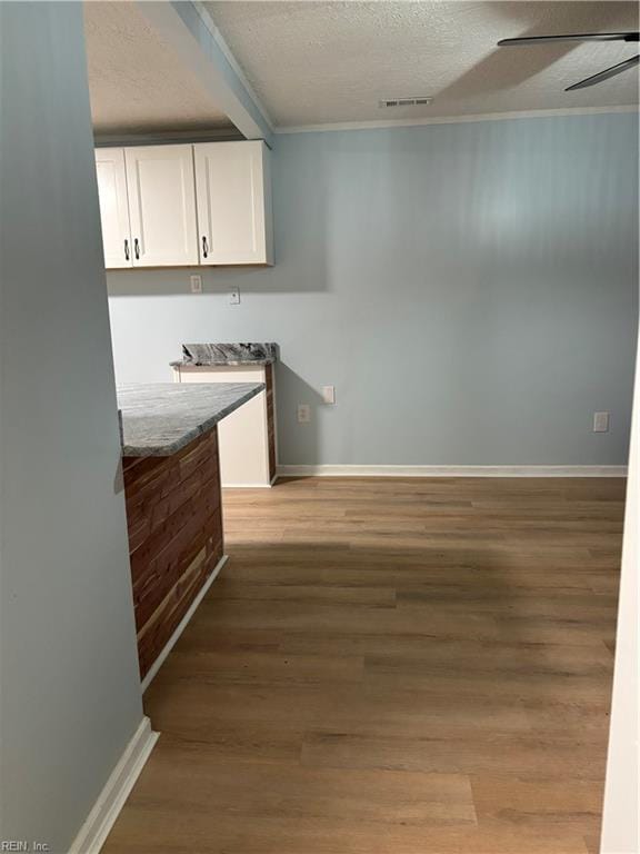 kitchen with light stone countertops, light wood-type flooring, a textured ceiling, ceiling fan, and white cabinetry