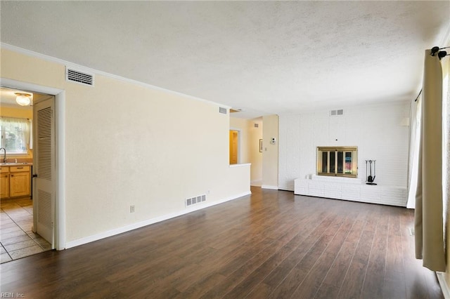 unfurnished living room featuring dark hardwood / wood-style flooring, a brick fireplace, ornamental molding, a textured ceiling, and sink