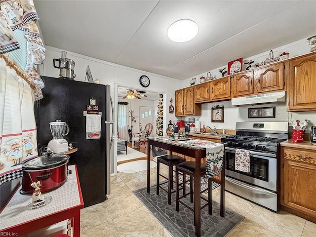 kitchen featuring black refrigerator, sink, stainless steel gas range, ceiling fan, and light tile patterned floors