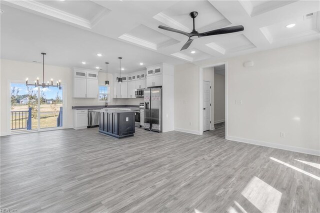 unfurnished living room featuring ornamental molding, coffered ceiling, ceiling fan with notable chandelier, beam ceiling, and light hardwood / wood-style flooring