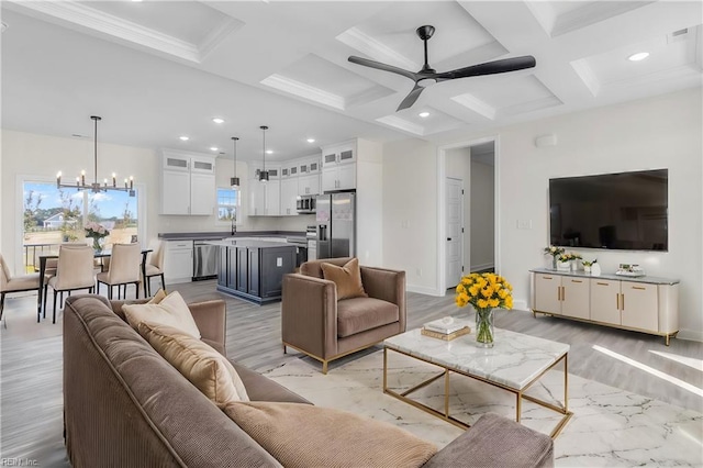 living room with coffered ceiling, ceiling fan with notable chandelier, crown molding, light wood-type flooring, and beam ceiling