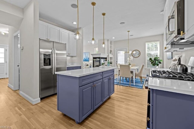 kitchen featuring pendant lighting, blue cabinetry, appliances with stainless steel finishes, light hardwood / wood-style floors, and white cabinetry