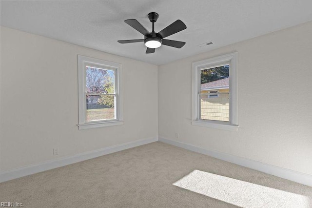 carpeted spare room with ceiling fan and plenty of natural light