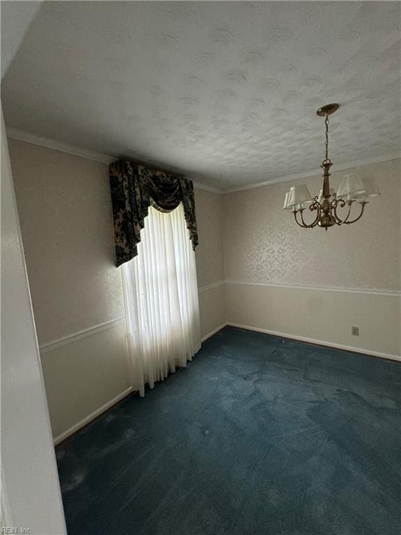 empty room with dark colored carpet, ornamental molding, a textured ceiling, and an inviting chandelier