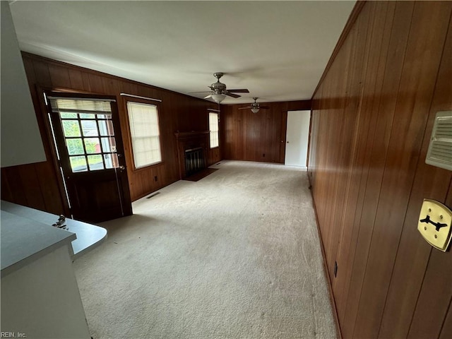 unfurnished living room with light carpet, ceiling fan, and wooden walls