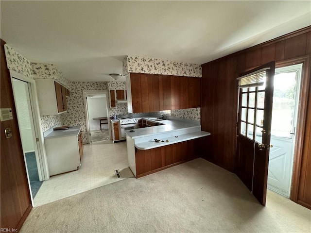 kitchen with wood walls, kitchen peninsula, white stove, and light carpet