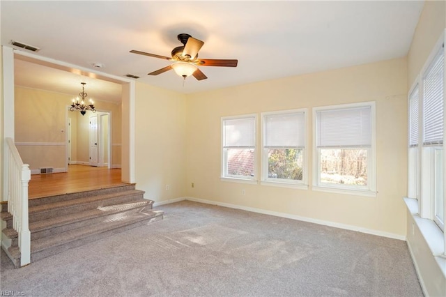 empty room with plenty of natural light, light colored carpet, and ceiling fan with notable chandelier