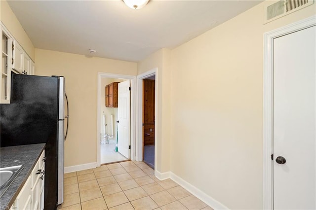 kitchen with stainless steel fridge, white cabinetry, sink, and light tile patterned floors