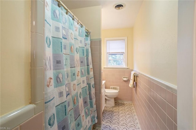 bathroom featuring a shower with shower curtain, toilet, and tile walls