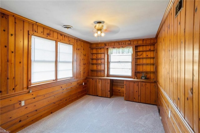 unfurnished office featuring light carpet, built in shelves, crown molding, and wood walls