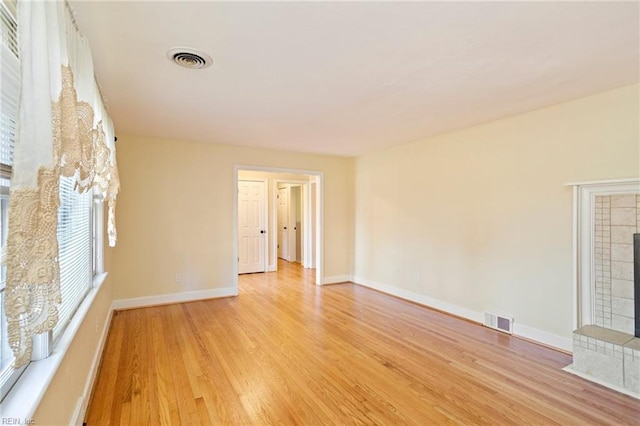 empty room with a tiled fireplace and light hardwood / wood-style flooring