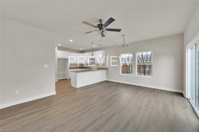 unfurnished living room featuring ceiling fan with notable chandelier, light hardwood / wood-style flooring, and a wealth of natural light