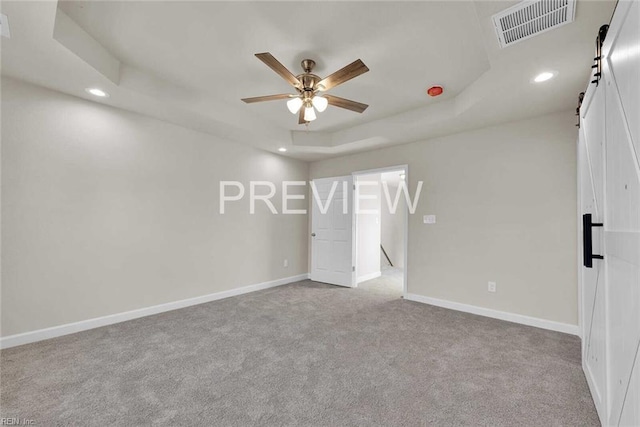 unfurnished bedroom featuring ceiling fan, a barn door, a raised ceiling, and light colored carpet