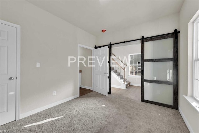 carpeted spare room featuring plenty of natural light and a barn door