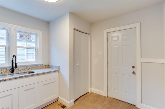 kitchen with light stone counters, white cabinetry, sink, and light hardwood / wood-style flooring