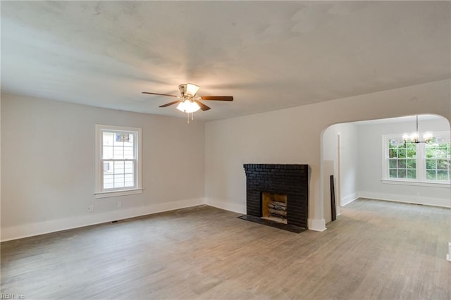 unfurnished living room featuring light wood-type flooring, ceiling fan with notable chandelier, and a brick fireplace