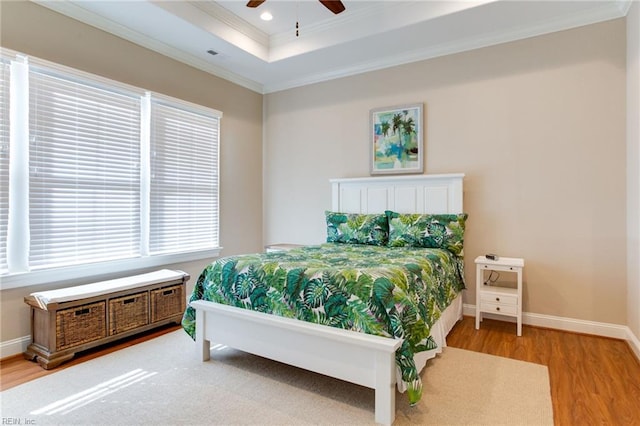 bedroom featuring hardwood / wood-style flooring, ceiling fan, ornamental molding, and a tray ceiling