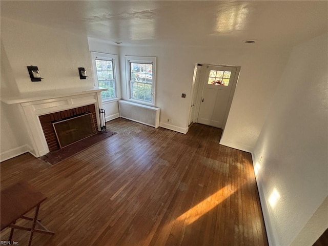 living room with dark wood-type flooring, radiator, and a brick fireplace