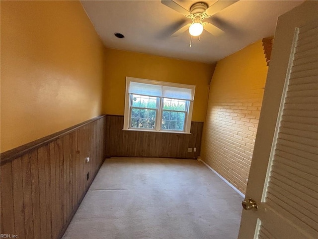 carpeted empty room with wooden walls, ceiling fan, and brick wall