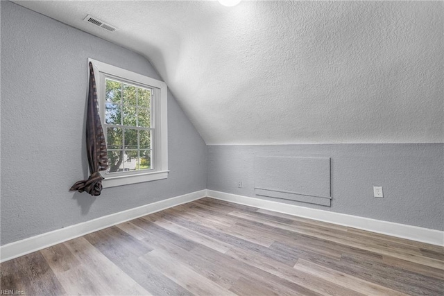 additional living space featuring a textured ceiling, light hardwood / wood-style floors, and vaulted ceiling