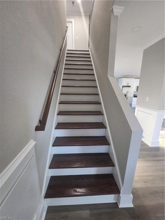 stairway with wood-type flooring and crown molding