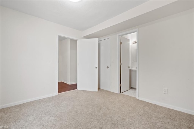 unfurnished bedroom with ensuite bathroom, a closet, and light colored carpet