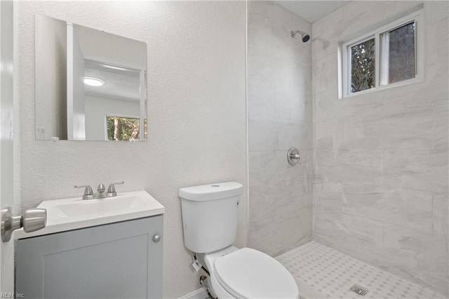 bathroom featuring a tile shower, vanity, and toilet