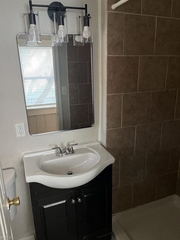 bathroom with a tile shower, vanity, and toilet