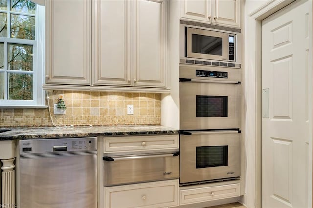 kitchen with decorative backsplash, cream cabinetry, stainless steel appliances, and dark stone countertops