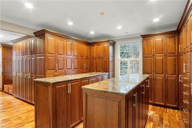 kitchen with light wood-type flooring, a center island, light stone countertops, and ornamental molding