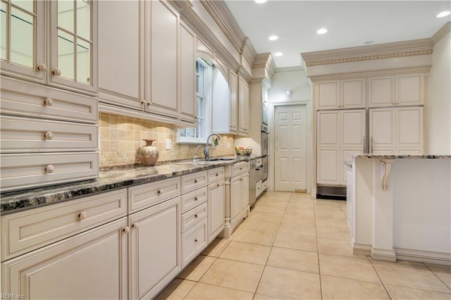 kitchen featuring crown molding, sink, light tile patterned floors, dark stone countertops, and cream cabinetry