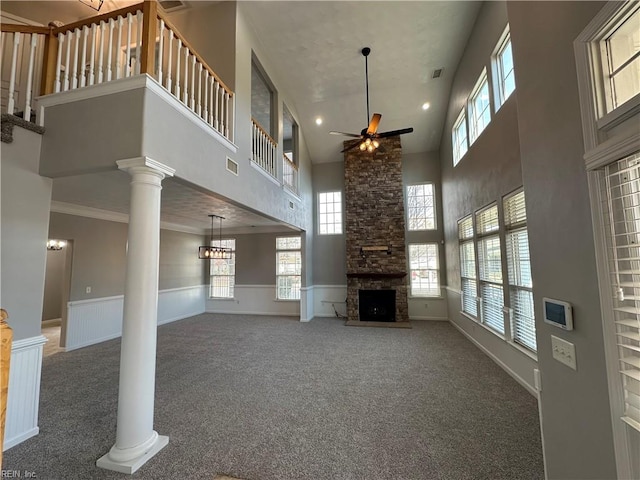 unfurnished living room featuring a towering ceiling, dark carpet, ornate columns, ceiling fan, and a stone fireplace