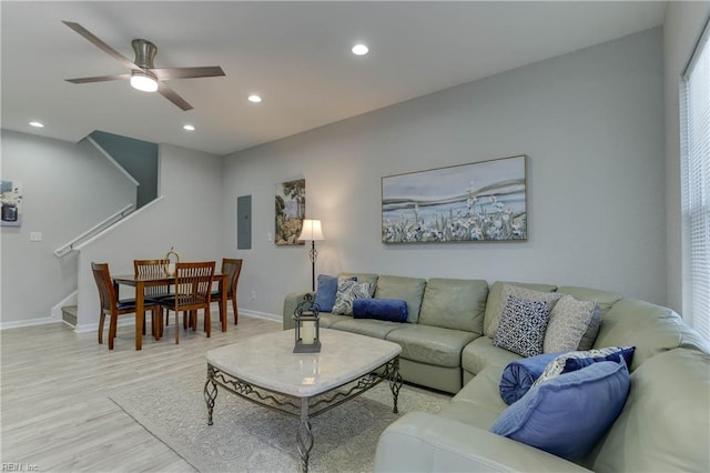 living room with electric panel, ceiling fan, and light wood-type flooring