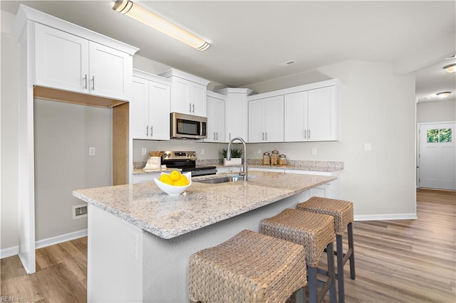 kitchen featuring white cabinets, stainless steel appliances, a kitchen island with sink, and sink