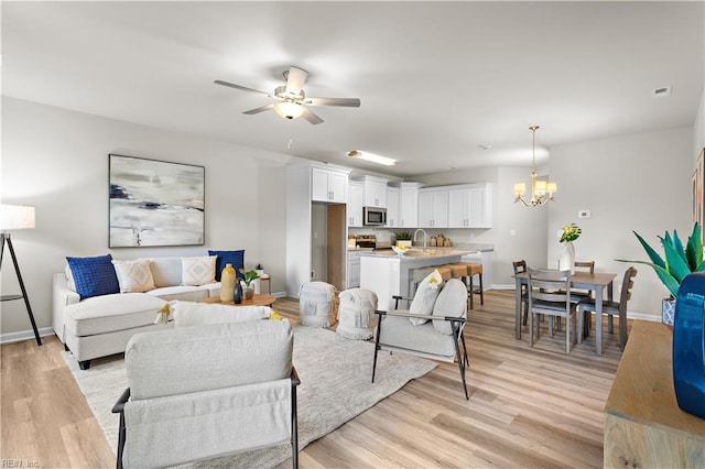 living room with ceiling fan with notable chandelier, light wood-type flooring, and sink